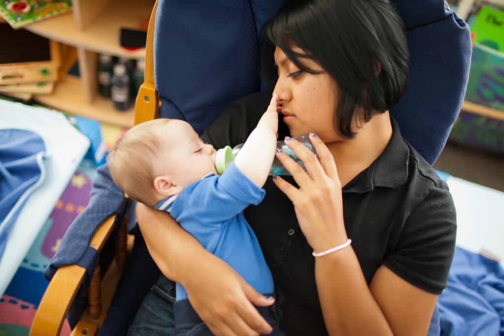 A child care worker holding an infant and feeding them with a bottle