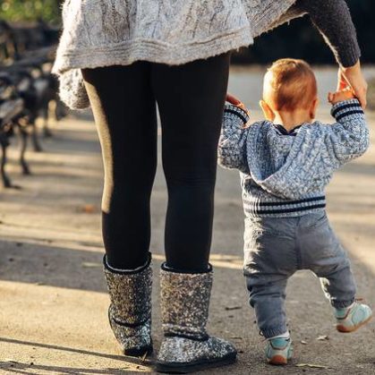Mother holding toddler's hands as they walk