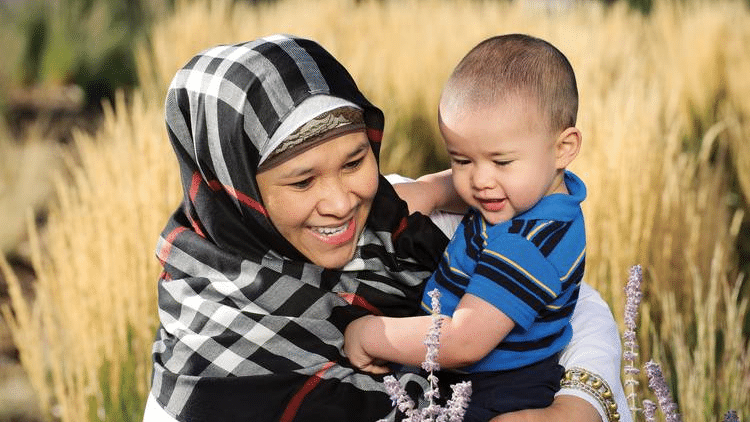 A woman with a religious head covering holding a baby boy.